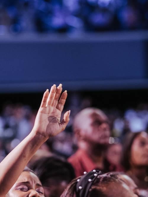 Placeholder: portrait-orientation photo of the congregation praying together, heads bowed, unified moment of worship.