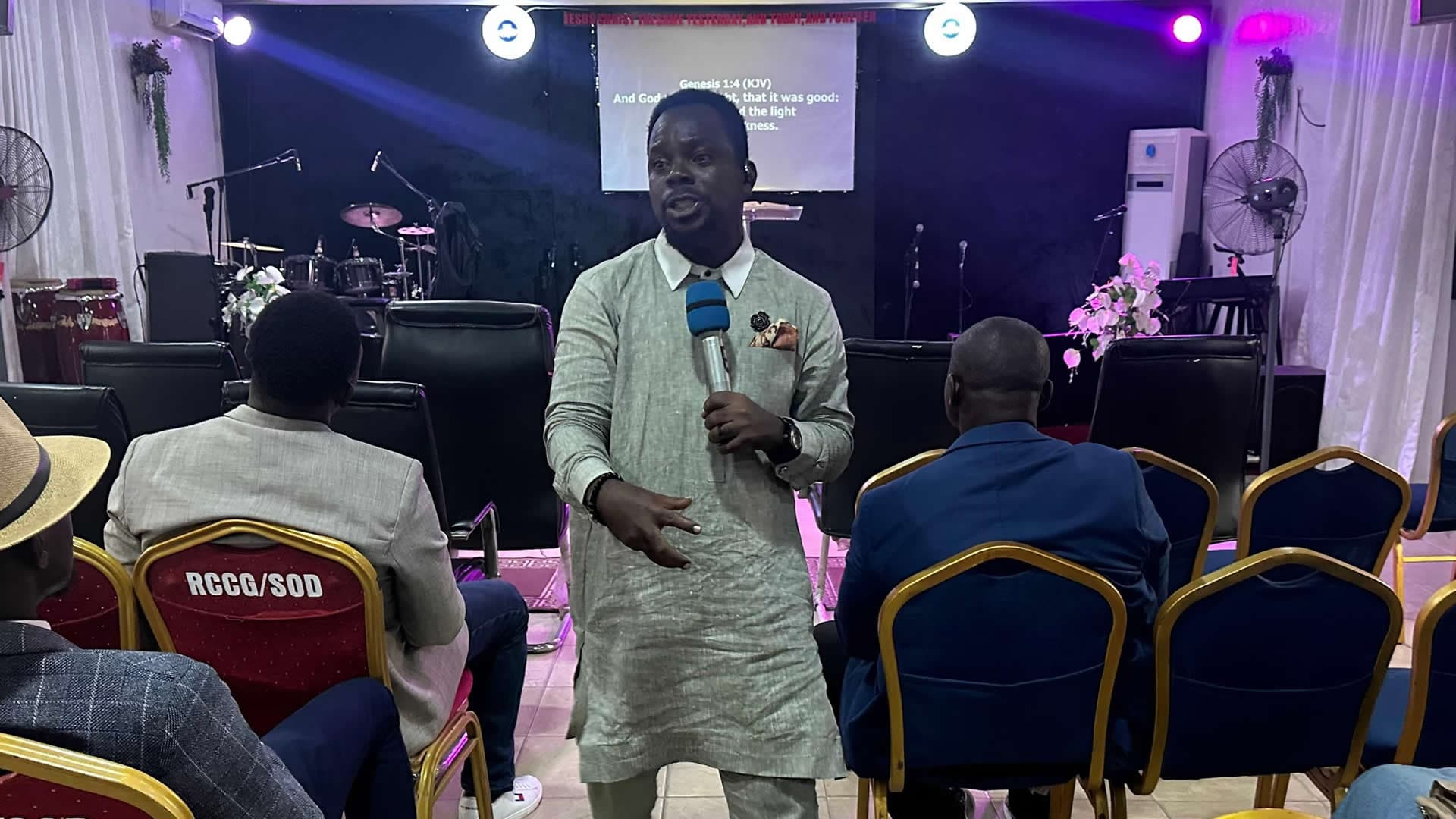 Placeholder: wide photo of the pastor mid-message on the main stage, warm gold stage lighting, congregation visible in soft focus foreground.